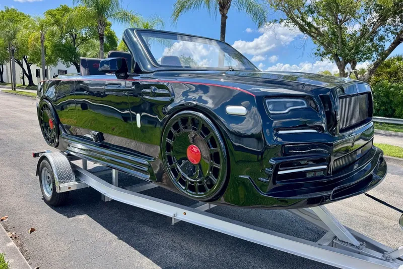 Slide: The Image of 2025 Watersports Car Series R on trailer, sleek black design, convertible, palm trees in background. - 7