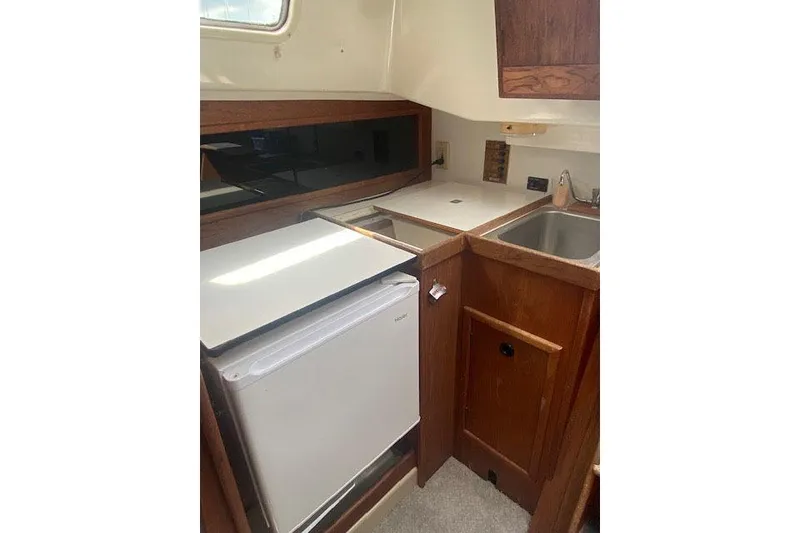 Slide: The Image of 1977 C&C 29 sailboat galley with compact fridge, sink, and wooden cabinetry. - 8