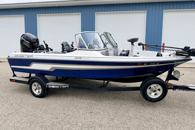 The Image of 2012 Skeeter SL 185 boat with Mercury engine, parked on a trailer near blue building. - 0