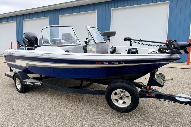 Slide: The Image of 2012 Skeeter SL 185 boat on trailer, blue and white, parked near a blue building. - 2