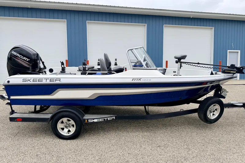 Slide: The Image of 2012 Skeeter SL 185 boat with Mercury engine on trailer, parked near blue building. - 4