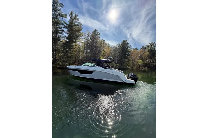 The Image of 2024 Cruisers Yachts 38 GLS OB on a serene lake, surrounded by lush trees. - 0