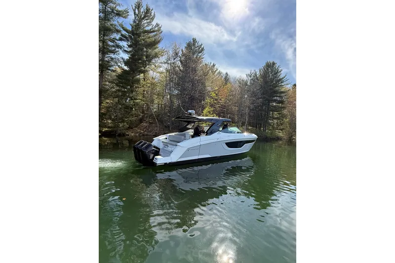 Slide: The Image of 2024 Cruisers Yachts 38 GLS OB on a serene lake, surrounded by lush trees. - 1