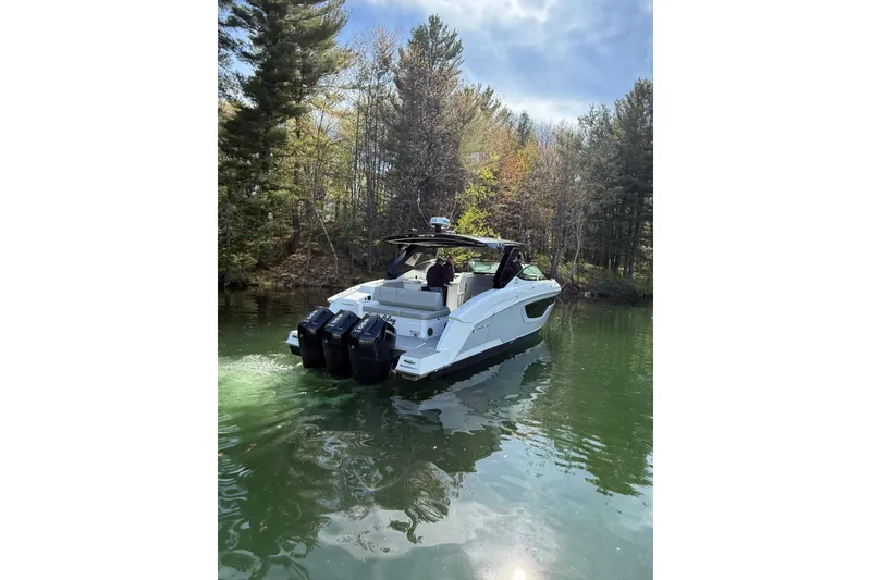Slide: The Image of 2024 Cruisers Yachts 38 GLS OB on a serene lake, surrounded by lush trees. - 2