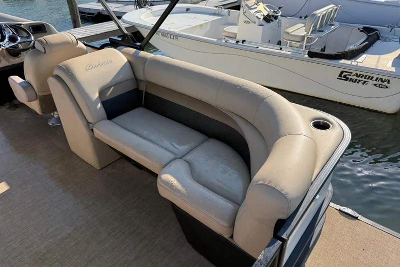 Slide: The Image of 2021 Barletta C22QC pontoon boat with beige seating and cup holder, docked beside another boat. - 16