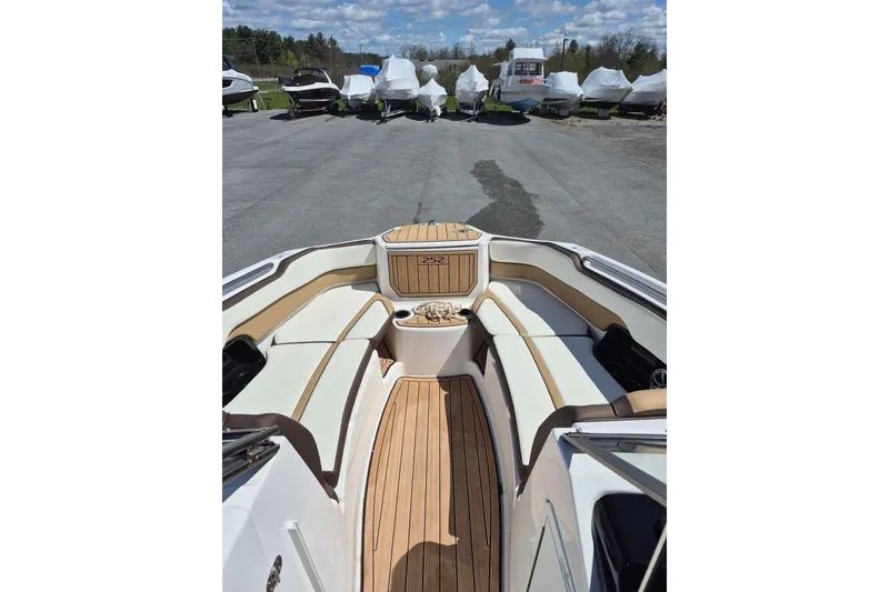 Slide: The Image of 2021 Yamaha Boats 252SE interior with sleek seating and wood finish, parked outdoors. - 10