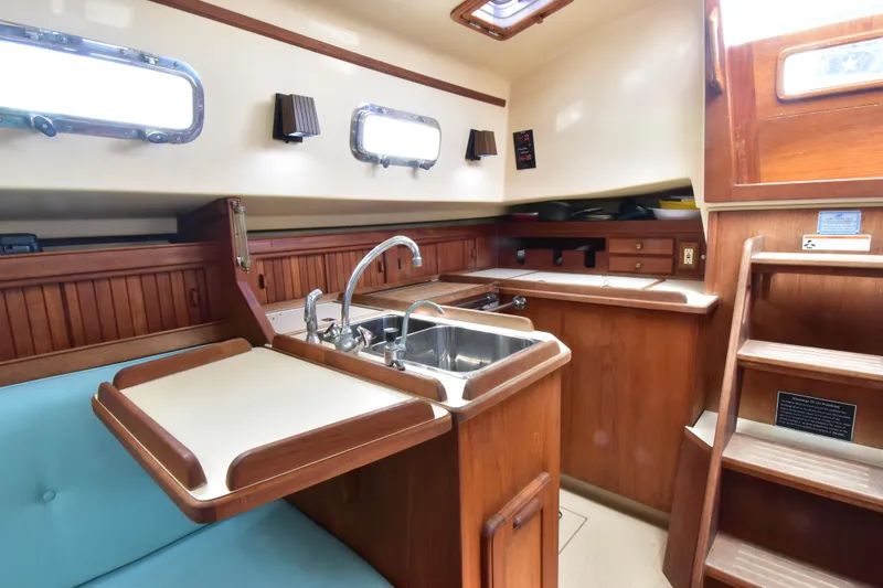 Slide: The Image of Interior of 1994 Island Packet 32 sailboat, featuring a compact wooden kitchen area. - 13