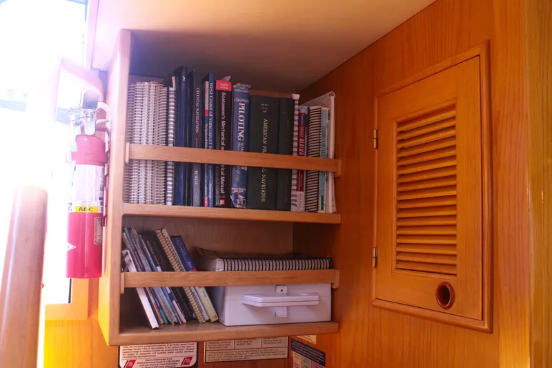 Slide: The Image of Bookshelf with navigation books and fire extinguisher on 1999 Grand Alaskan Pilothouse yacht. - 107