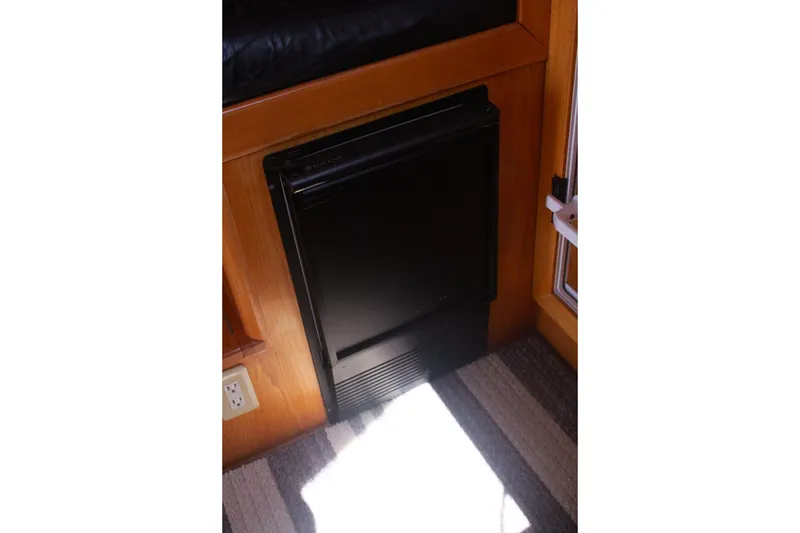 Slide: The Image of Black mini fridge in 1999 Grand Alaskan Pilothouse interior, wooden paneling, carpeted floor. - 112