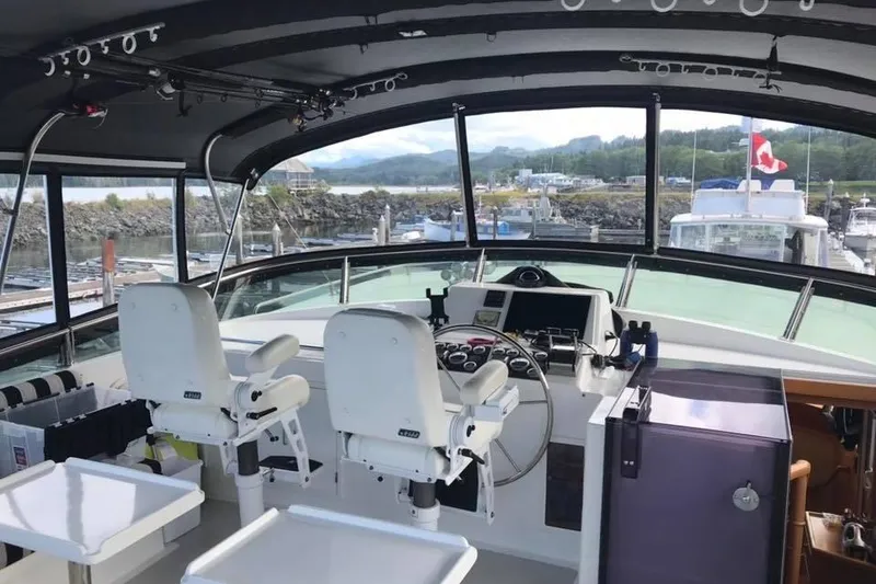 Slide: The Image of 1999 Grand Alaskan Pilothouse interior with helm, chairs, and panoramic marina view. - 21