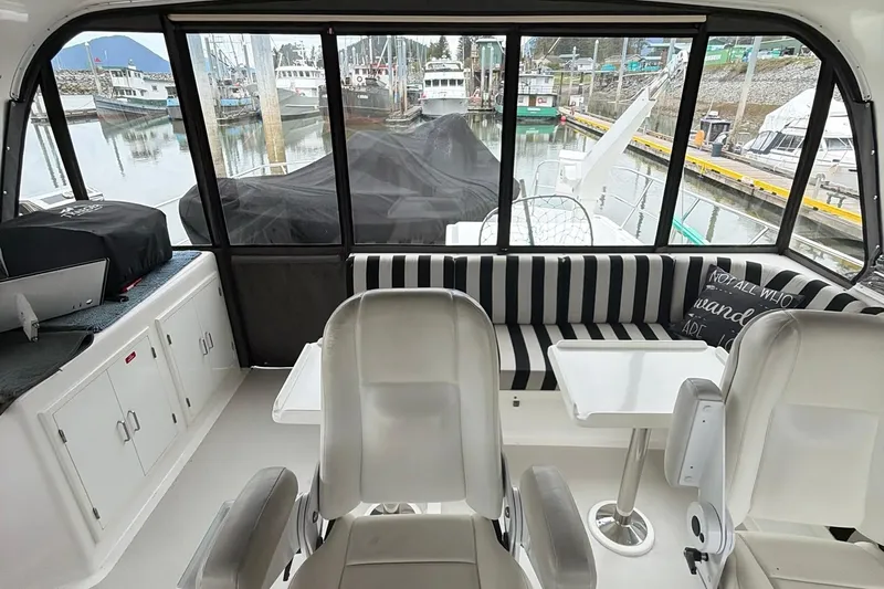 Slide: The Image of Interior of a 1999 Grand Alaskan Pilothouse yacht with striped seating and marina view. - 24