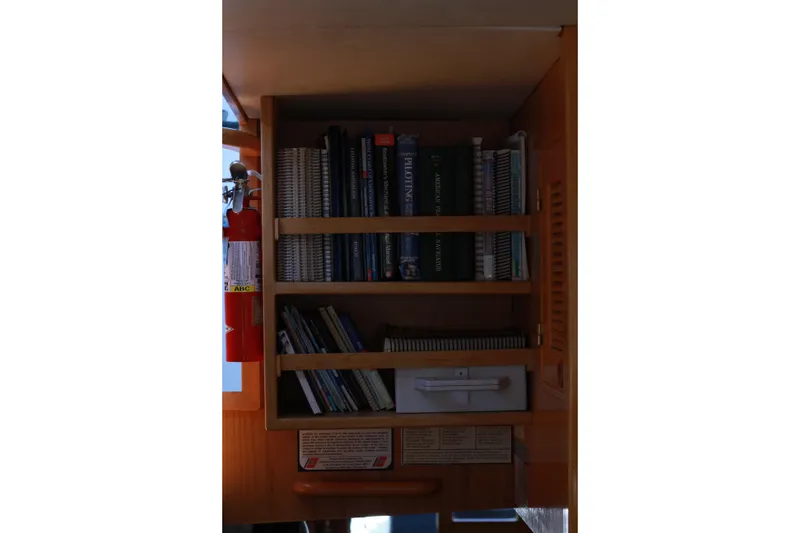 Slide: The Image of Bookshelf with navigation books and fire extinguisher on 1999 Grand Alaskan Pilothouse yacht. - 83