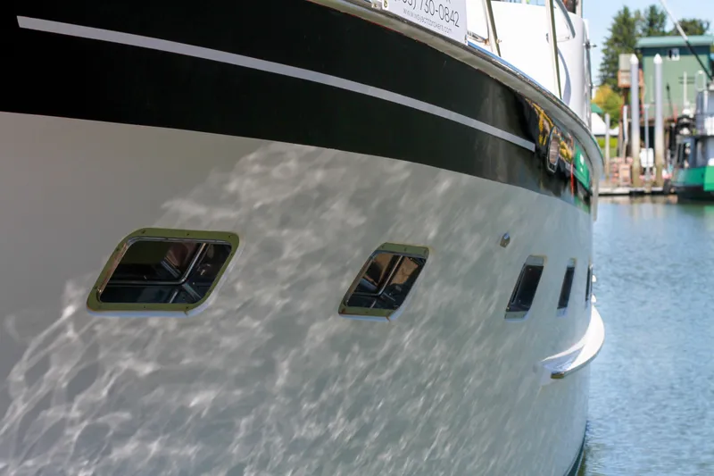 Slide: The Image of 1999 Grand Alaskan Pilothouse yacht reflecting sunlight on water, docked at marina. - 87