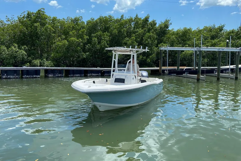 Slide: The Image of 2023 Tidewater 220 LXF boat on calm water near a dock, surrounded by lush greenery. - 5