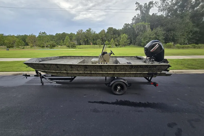 The Image of 2026 Tracker Grizzly 2072 CC boat on trailer, parked on asphalt with green landscape background. - 0