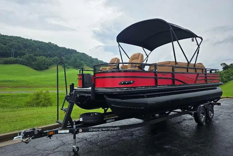 Slide: The Image of 2026 Ranger 220F pontoon boat on trailer, red and black design, parked on scenic road. - 1