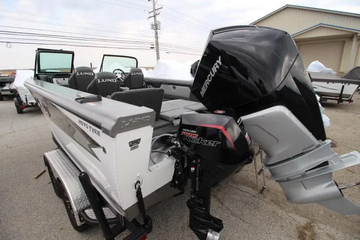 Slide: The Image of 2026 Lund 2075 Tyee boat with Mercury outboard motor, parked outdoors. - 2