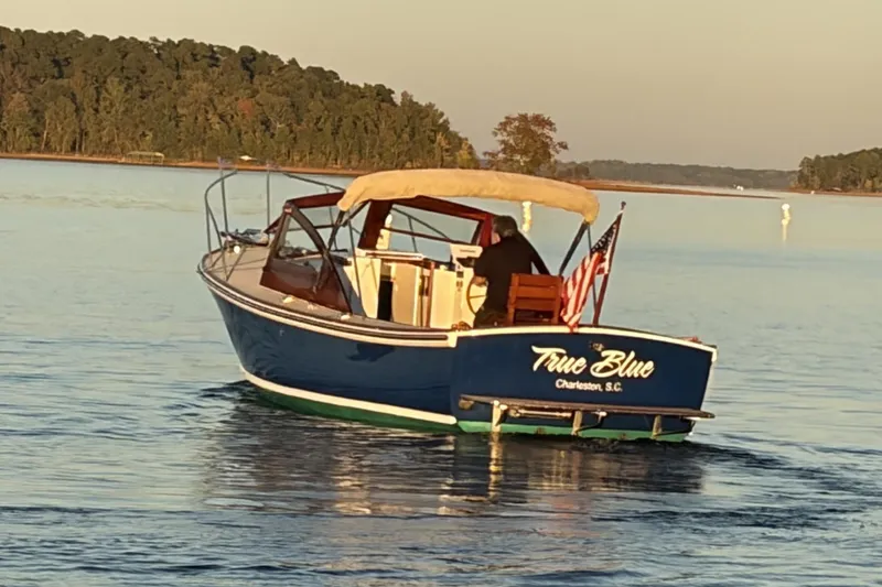 Slide: The Image of 1973 Dyer 29 Bass Boat "True Blue" cruising on calm waters near a forested shoreline. - 4
