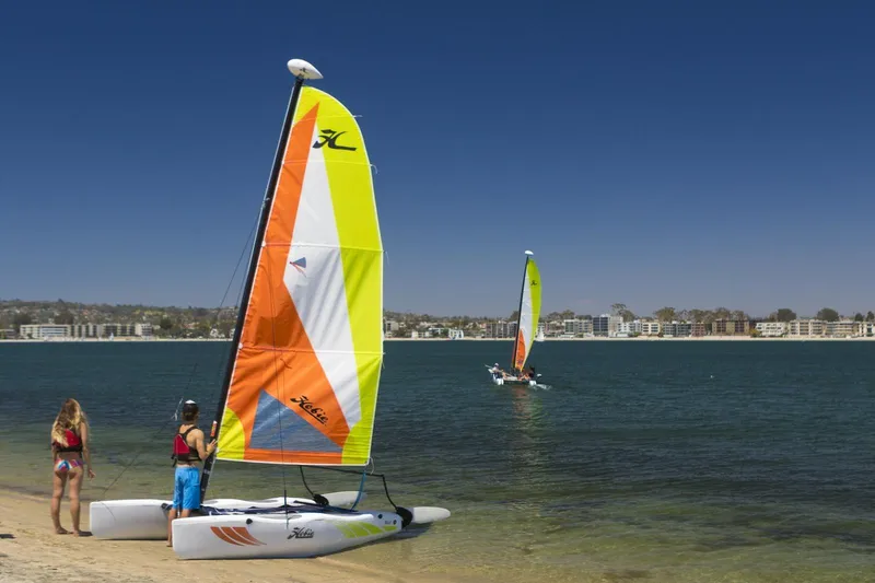 The Image of 2023 Hobie Cat Wave sailboats on a sunny beach with people preparing to sail. - 1