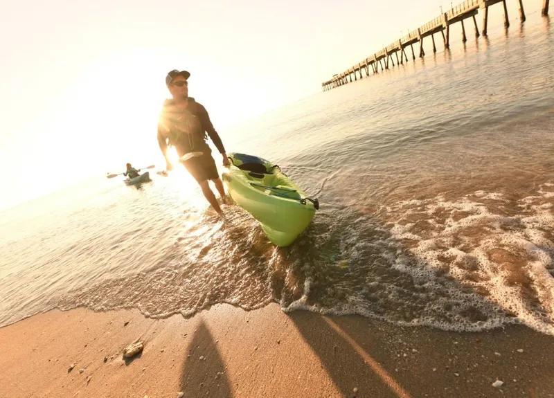 Slide: The Image of Man pulling Ocean Kayak Malibu 11.5 (2023) onto beach at sunrise. - 5