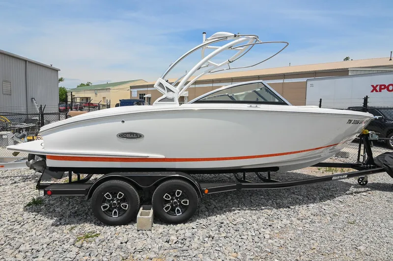 The Image of 2022 Cobalt CS22 boat on trailer, white with orange stripe, parked on gravel. - 0