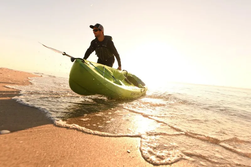 Slide: The Image of Man launching Ocean Kayak Malibu 9.5, 2023 model, into the ocean at sunrise. - 7