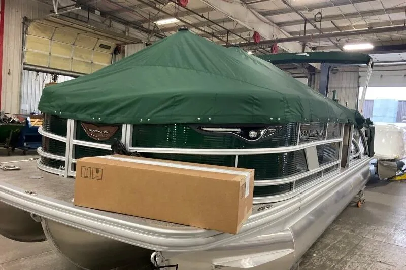 Slide: The Image of 2026 Bennington 24 M L-Bench pontoon boat with green cover in a warehouse. - 12