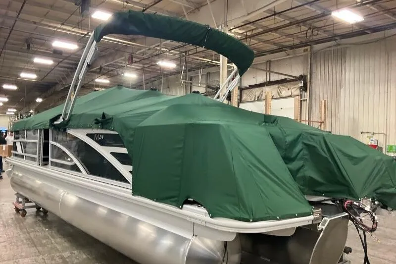 Slide: The Image of 2026 Bennington 24 M L-Bench pontoon boat with green cover in warehouse. - 13