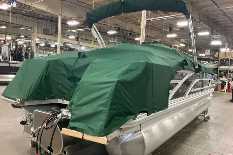 Slide: The Image of 2026 Bennington 24 M L-Bench pontoon boat with green cover in a warehouse. - 14