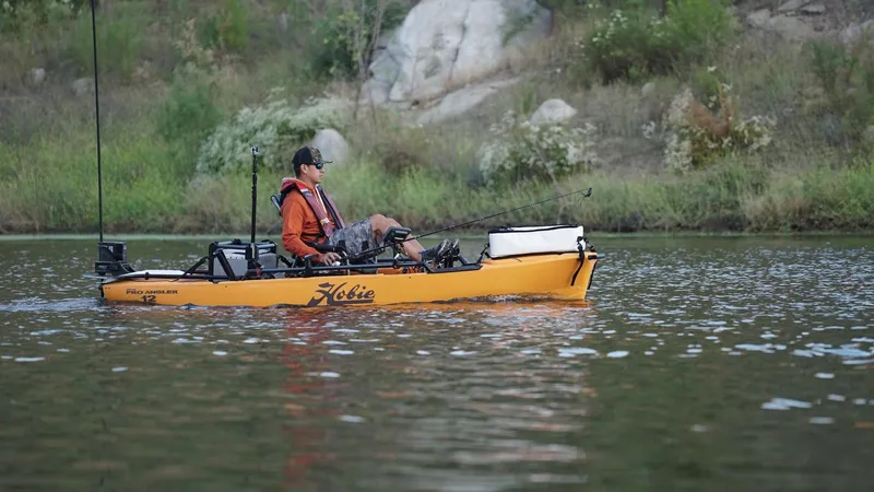 Slide: The Image of 2023 Hobie Pro Angler 12 kayak on a calm lake with a person fishing. - 1