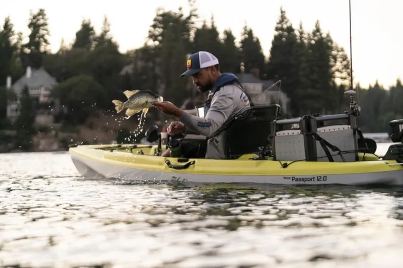 The Image of Man fishing from a 2023 Hobie Passport 12.0 kayak on a serene lake. - 0