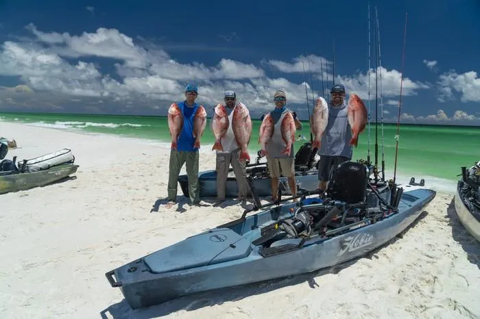 Slide: The Image of Four anglers with fish beside Hobie Mirage Pro Angler 14 kayaks on a beach, 2023 model. - 2