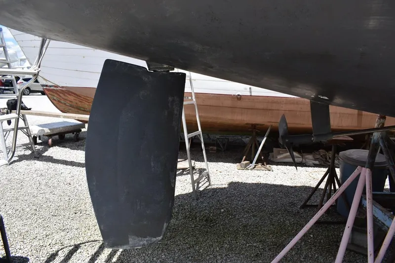 Slide: The Image of 2001 Catalina 310 sailboat keel and rudder in dry dock, gravel ground, maintenance setting. - 10
