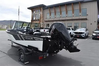 Slide: The Image of 2026 Lowe Fishing Machine 1675 WT boat with Mercury engine, parked outside a modern building. - 5