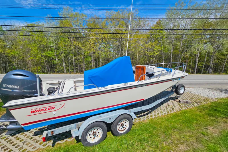 Slide: The Image of 1990 Boston Whaler OUTRAGE CUDDY boat on trailer, with Yamaha engine, parked outdoors. - 2