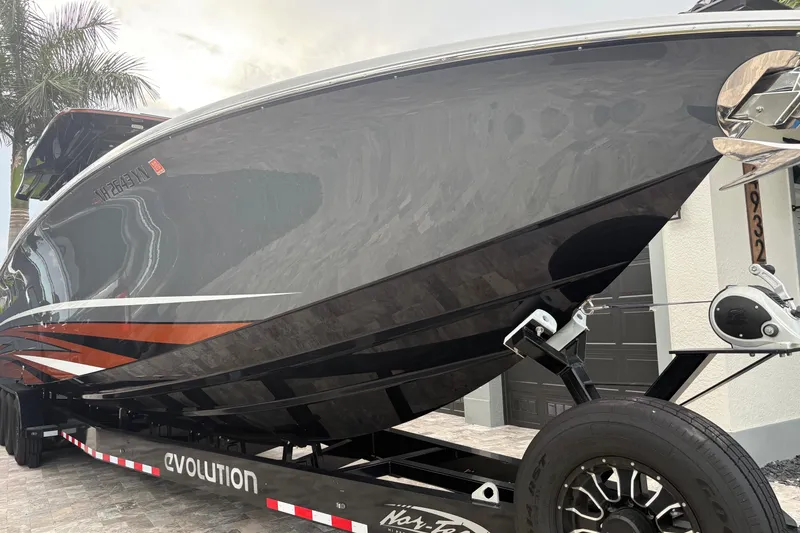 Slide: The Image of 2024 Nor-Tech 390 Sport Center Console boat on trailer, sleek black design with orange accents. - 2