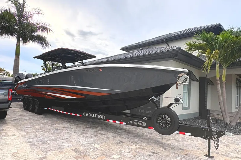 Slide: The Image of 2024 Nor-Tech 390 Sport Center Console boat on trailer, parked by a house with palm trees. - 3