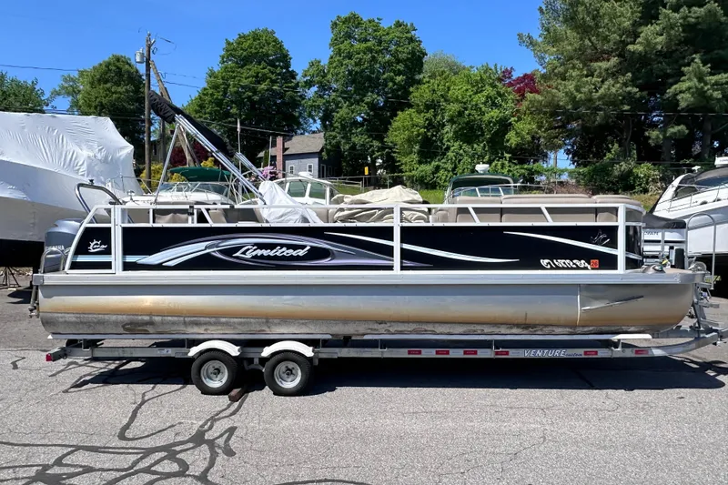 Slide: The Image of 2015 JC 24 Tri-Toon pontoon boat on trailer, parked outdoors with trees in background. - 2