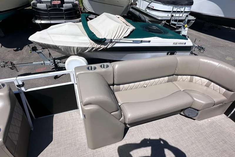 Slide: The Image of 2015 JC 24 Tri-Toon boat with beige seating and cup holders, parked near other boats. - 20