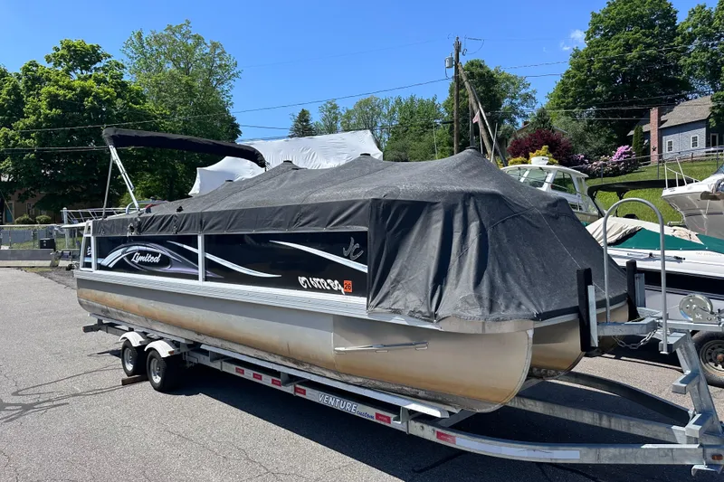 Slide: The Image of 2015 JC 24 Tri-Toon pontoon boat covered on a trailer, parked outdoors. - 26