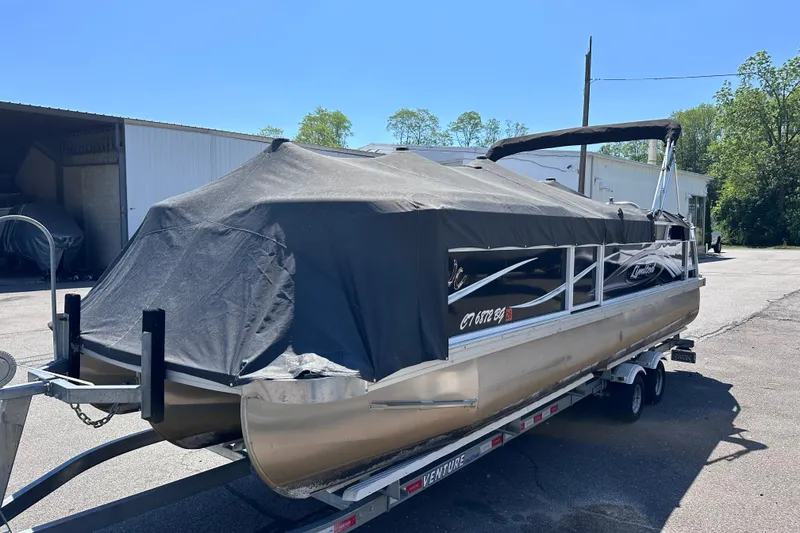 Slide: The Image of 2015 JC 24 Tri-Toon boat covered on trailer, parked outdoors. - 27
