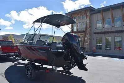 Slide: The Image of 2026 Lowe Fish & Ski 1700 boat with canopy, parked outside a building on a sunny day. - 9