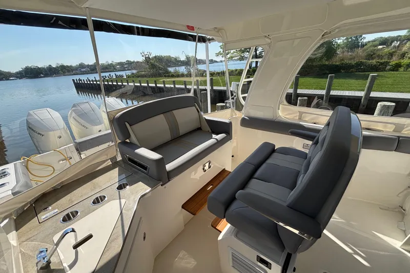 Slide: The Image of 2024 Boston Whaler 350 Realm interior with seating, docked by a scenic waterfront. - 9