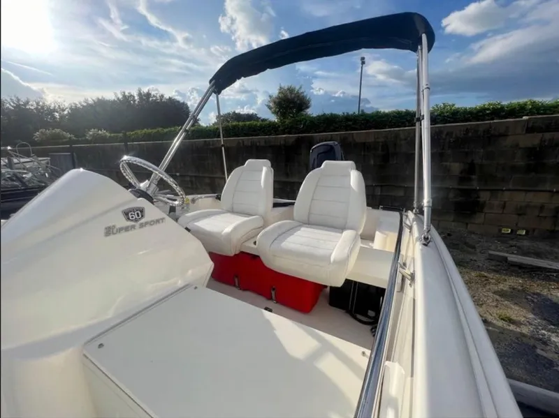 Slide: The Image of A 2018 Boston Whaler 150 Super Sport with two white seats and a blue sunshade. - 2