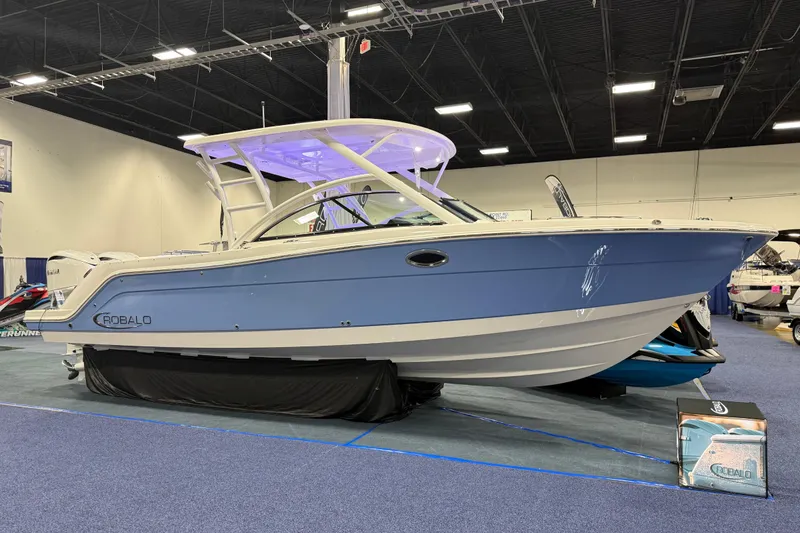 The Image of 2026 Robalo R317 Dual Console boat displayed indoors, featuring sleek blue and white design. - 0