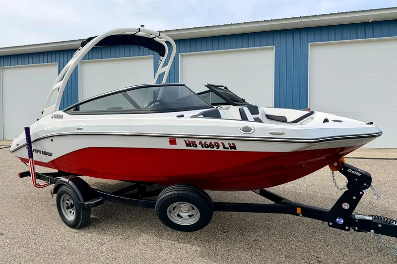 Slide: The Image of 2024 Yamaha AR195 boat with red hull on trailer, parked near blue building. - 1