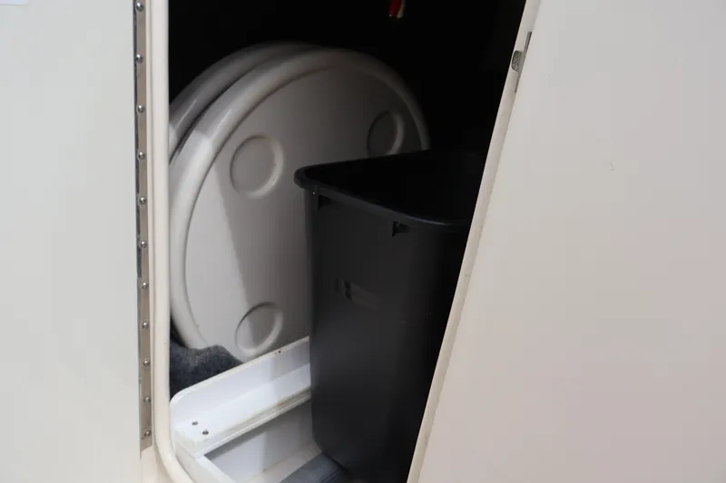 Slide: The Image of Storage compartment in a 2007 Sea Ray 220 Sundeck boat, featuring a black bin and round items. - 30
