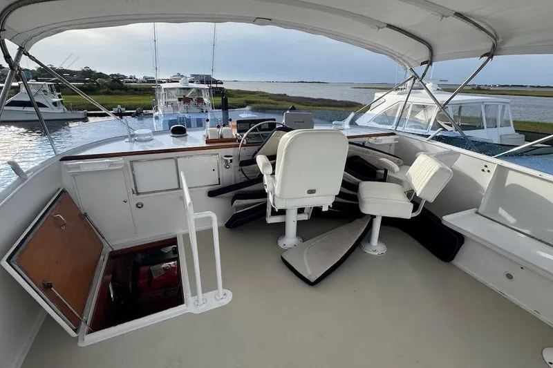 Slide: The Image of 1974 Burger 67 Motor Yacht helm with white seating and open hatch, docked by water. - 22
