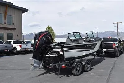 Slide: The Image of 2026 Lowe Fishing Machine 1875 boat on trailer, parked outdoors near trucks and building. - 10