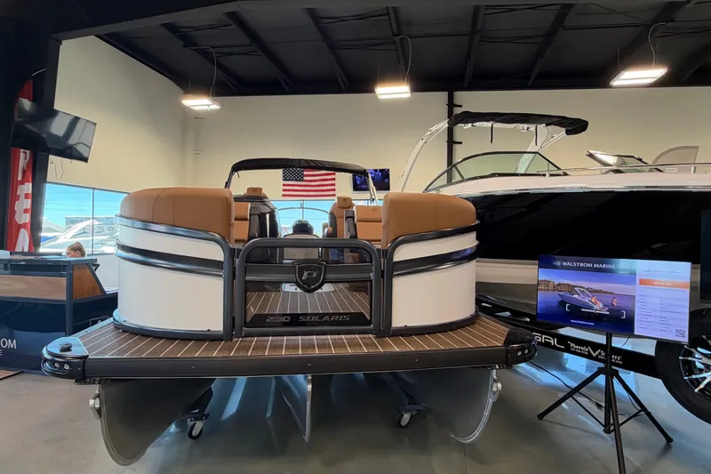 Slide: The Image of 2027 Premier 230 Solaris RF - CL pontoon boat displayed indoors with American flag backdrop. - 2